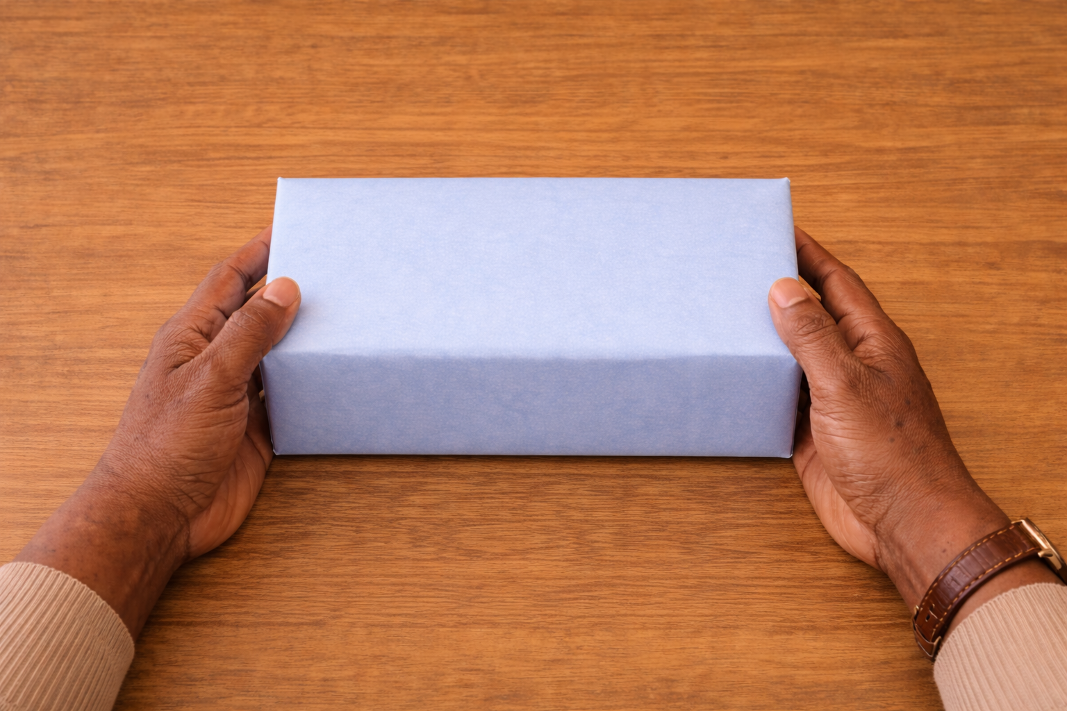Person holding a light blue gift wrapped rectangular box on a wooden surface