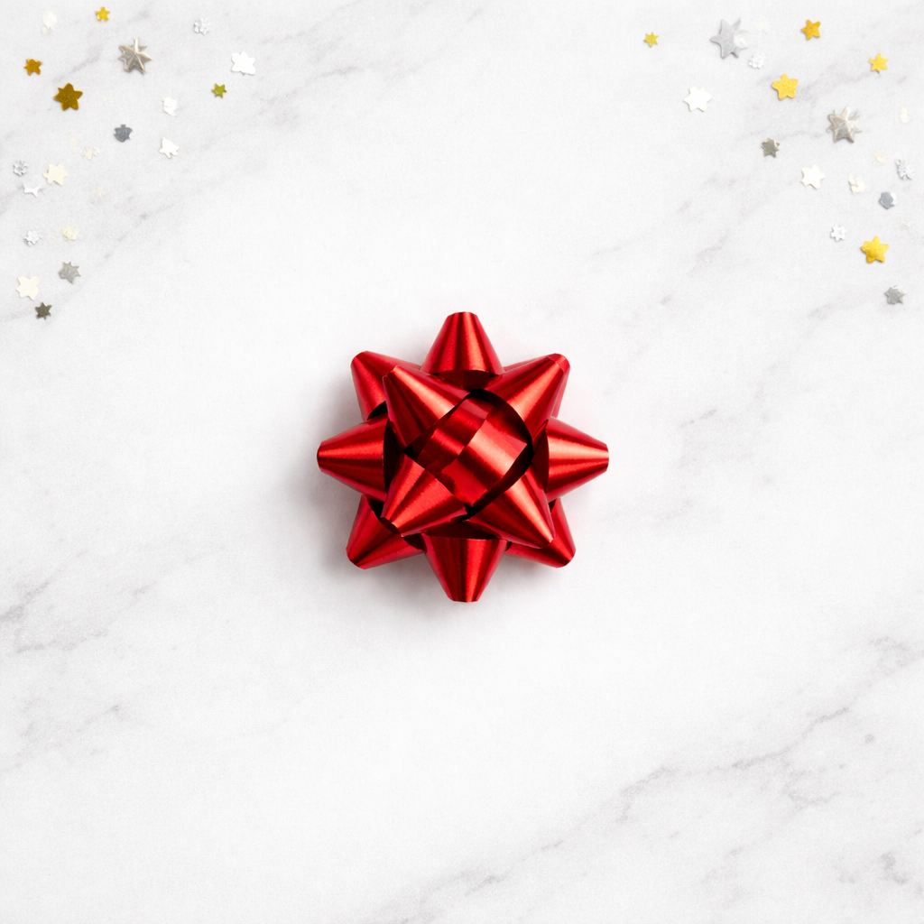 Red gift bow on a white marble surface with star-shaped confetti.