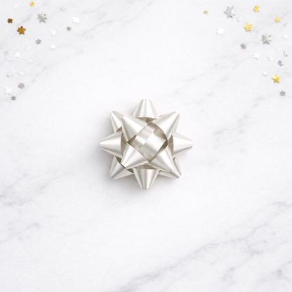 Silver gift bow on a white marble surface with star-shaped confetti.