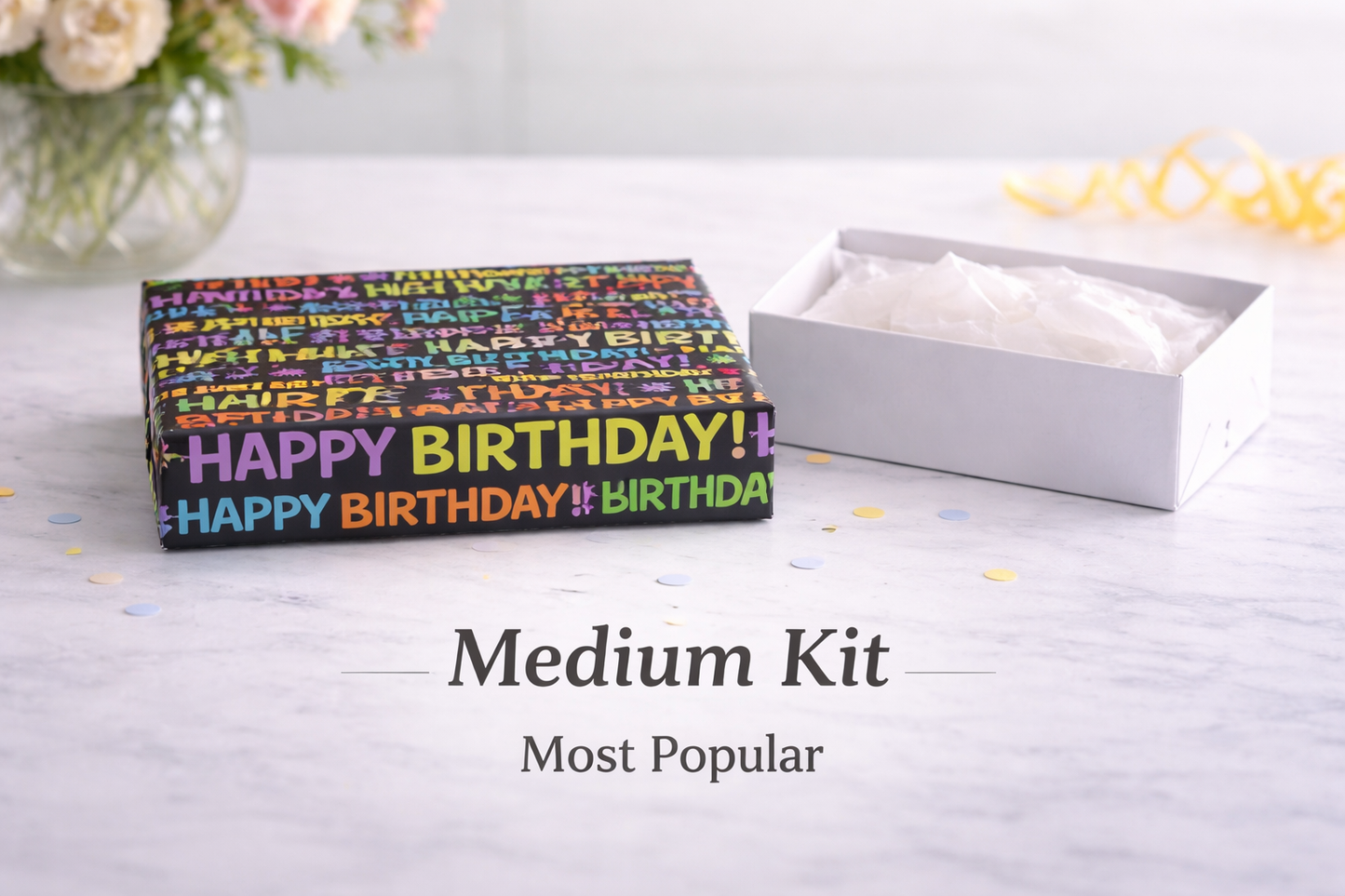 Box with 'Happy Birthday!' text on a light surface with flowers in the background